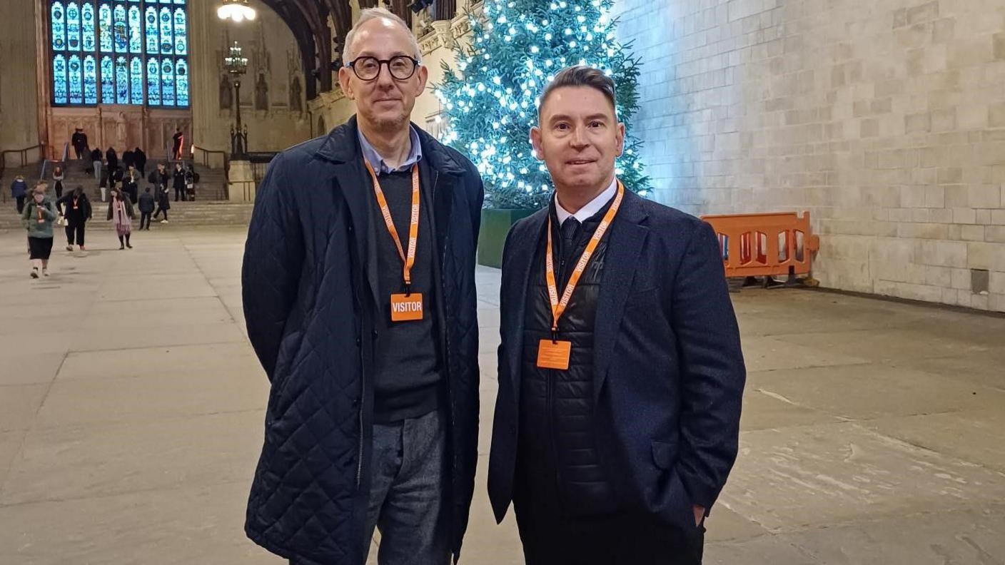 CEO of Winston's Wish, Fergus Crow standing with Mark at the House of Commons in it's main lobby wearing orange visitors lanyards and wearing dark clothes