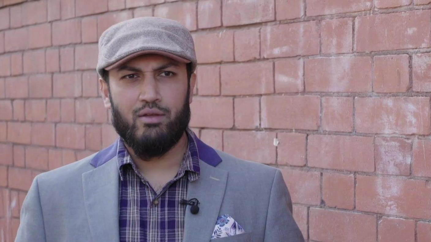 Mohi in a purple shirt, grey suit jacket and grey flat cap.