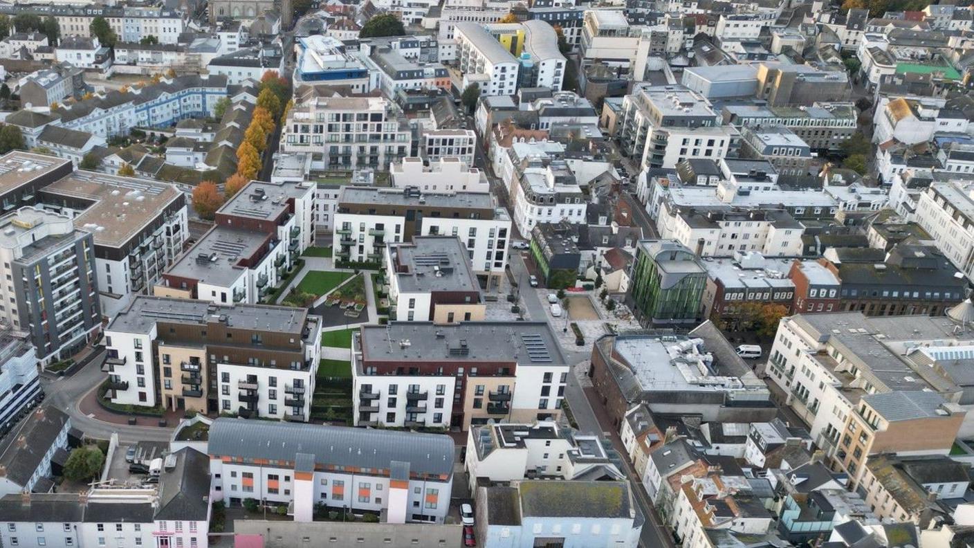 A drone shot of buildings and homes in St Helier in Jersey. The photo shows roof tops and a number of roads and trees between the buildings.