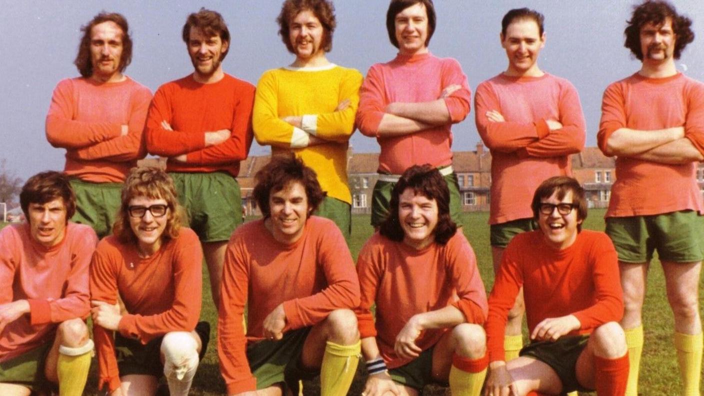 A dated looking picture of a group of men wearing red tops, green shorts and yellow socks for a football match all looking at the camera