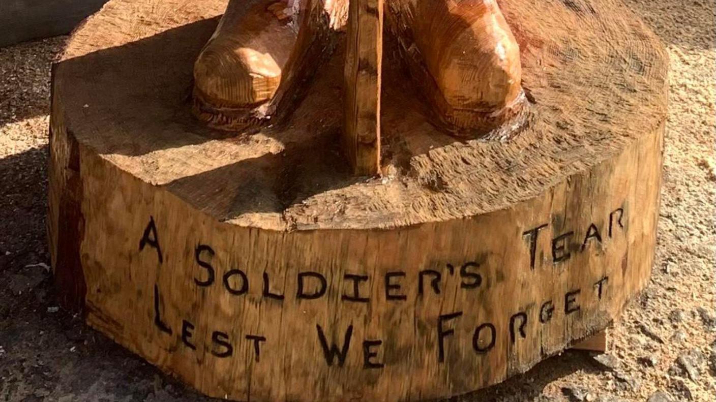 The bottom of a wooden sculpture with a message saying "A Soldier's Tear, lest we forget"