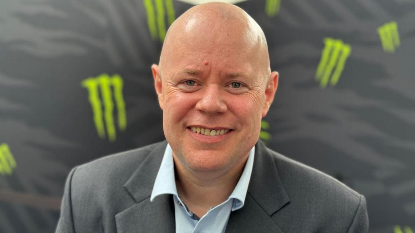 Geoff Pugh is bald and wearing a light blue shirt with a grey suit jacket.