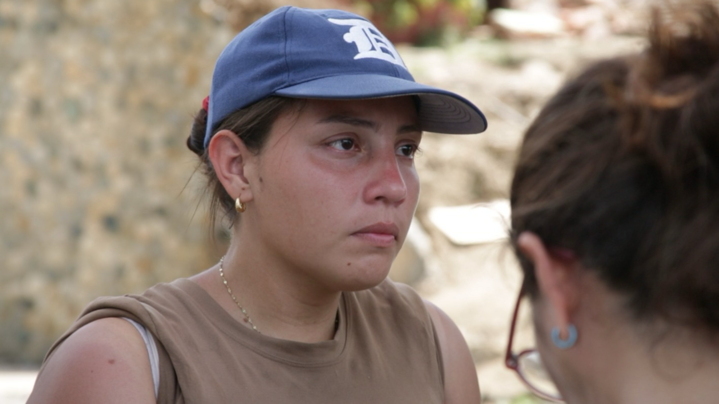 Andreina Valerio, in a blue baseball cap, stands in front of rubble