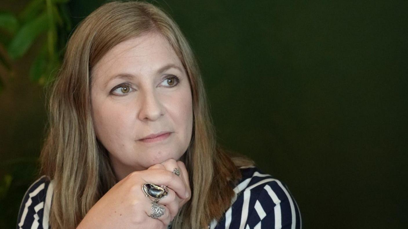 Kate Parrinder has long brown hair and is wearing a dark blue and white stripy top.