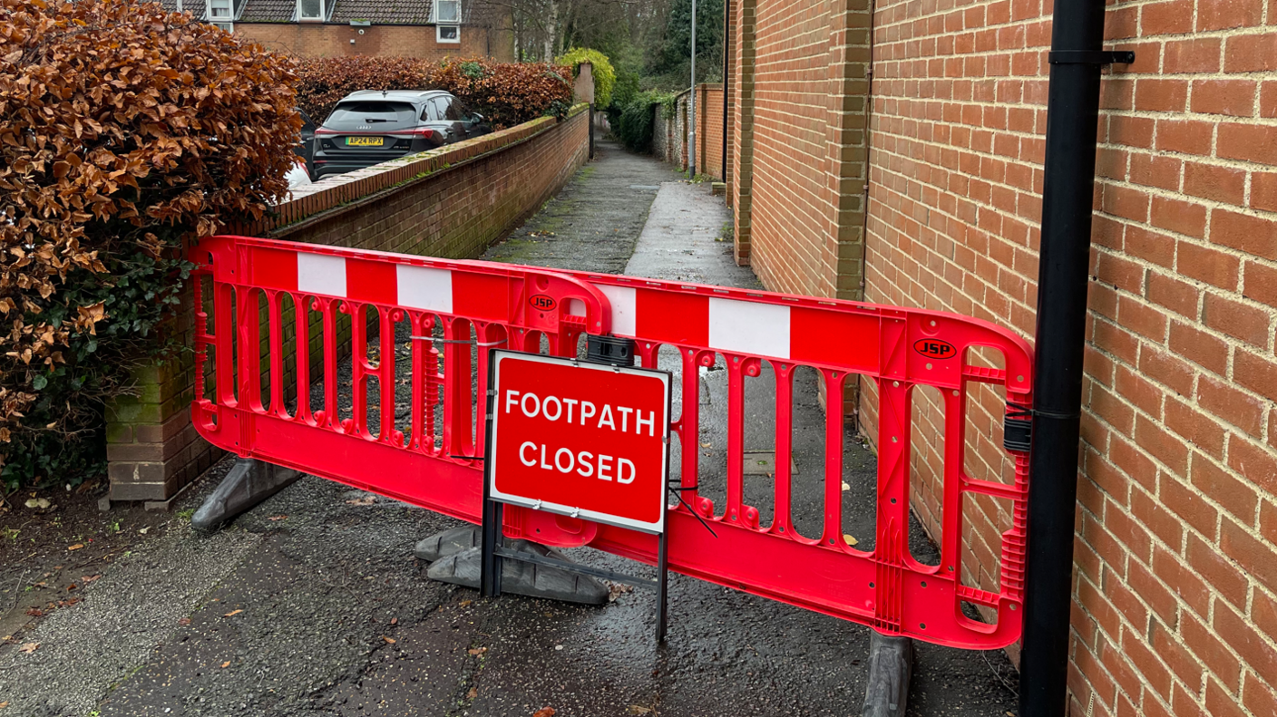 A red blockade and a sign saying footpath closed at the entrance to an alleyway 