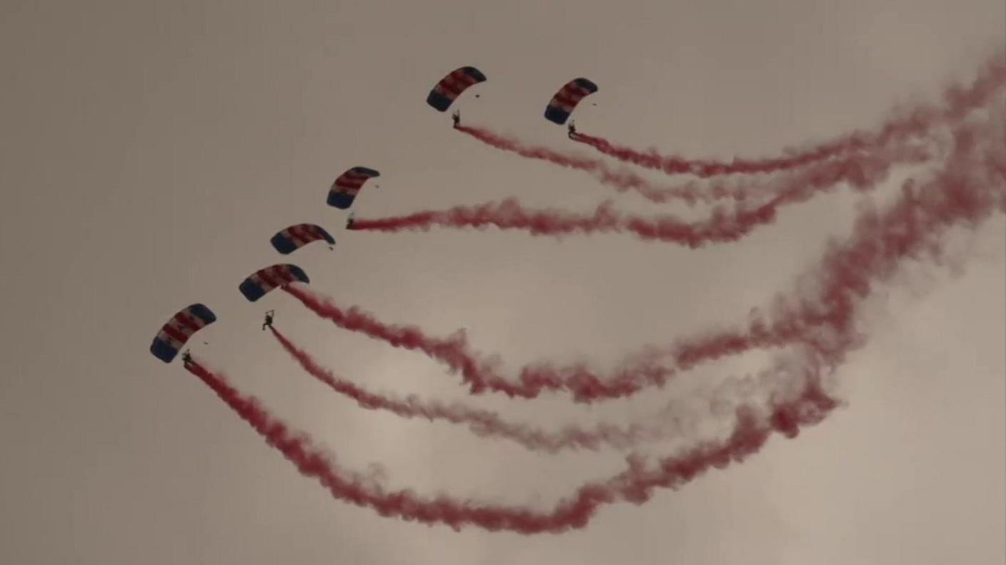 Parachutists in the sky with red smoke following behind them. 