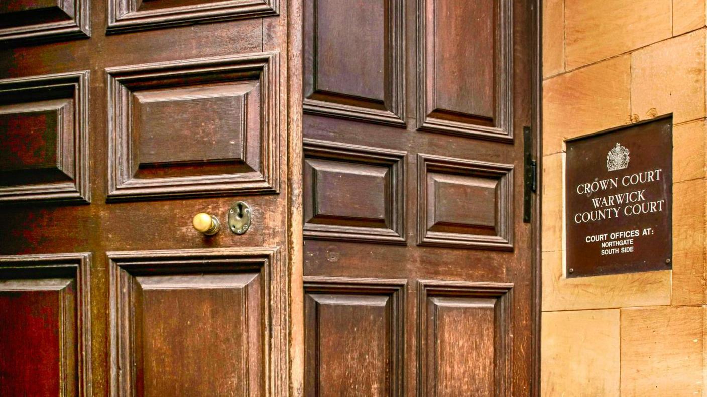 A door open at Warwick Crown Court with a Warwick Crown Court sign at the side of the building 