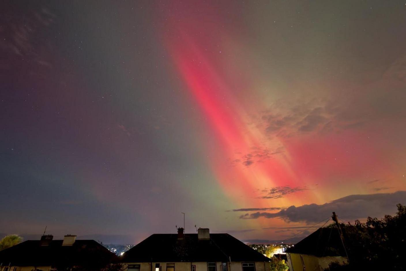 A row of houses with street lights and the aurora behind them. The aurora appears in red, green and pink.