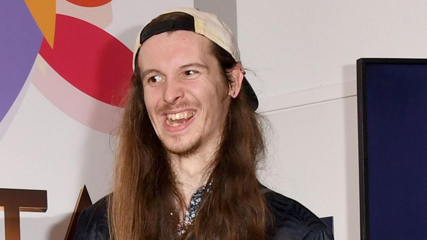 James Moore wearing a backwards white cap, smiling at the National Television Awards 2019