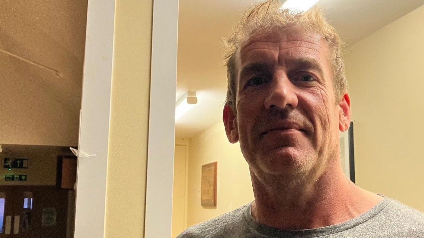 Alex wearing a grey T-shirt- looking into the camera 