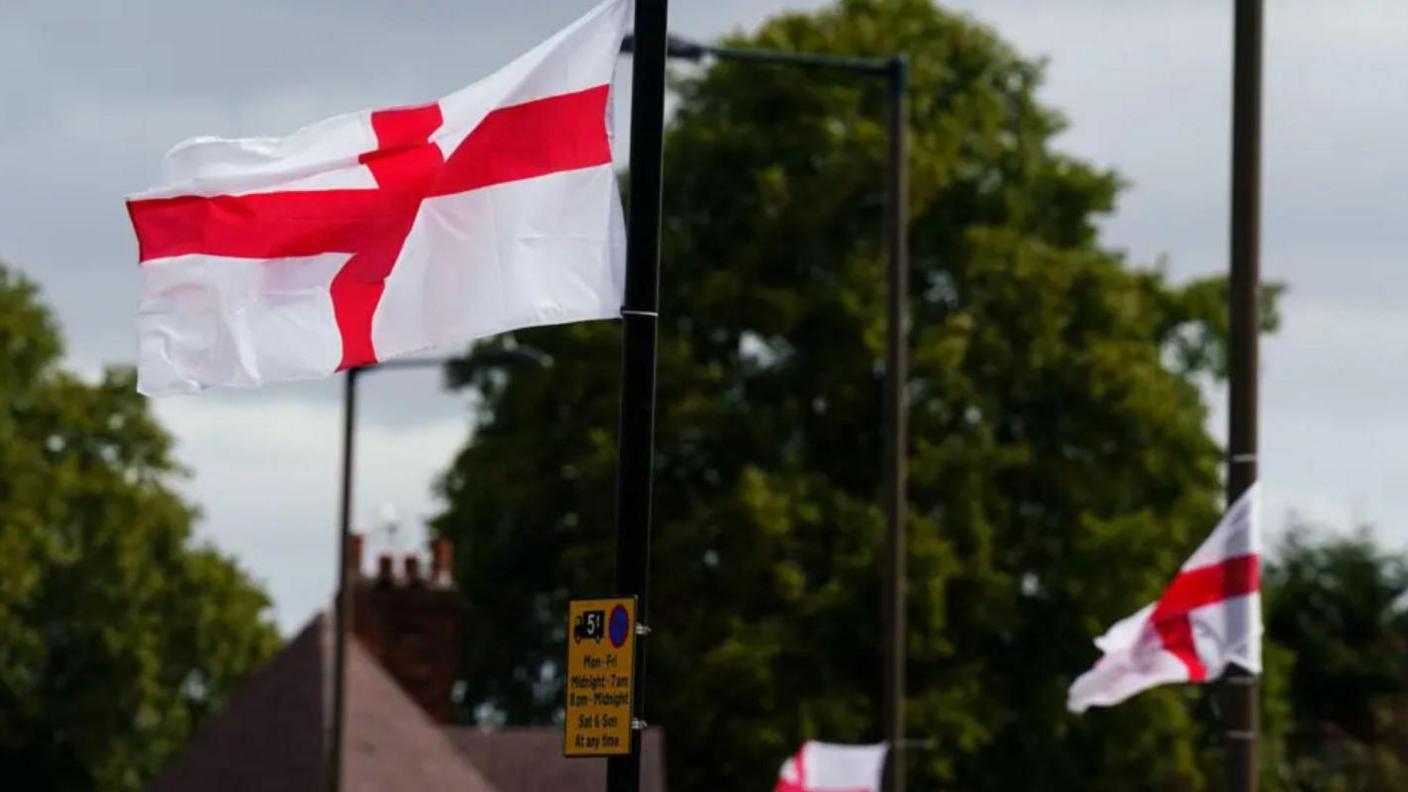 Two England flags hanging from lamp posts with trees in the background
