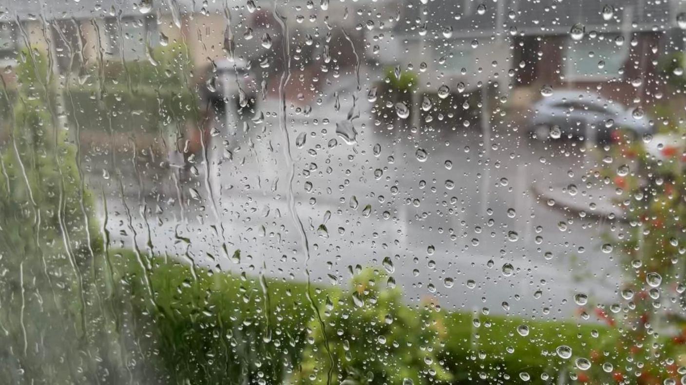 A residential street seen blurrily through a window covered in raindrops