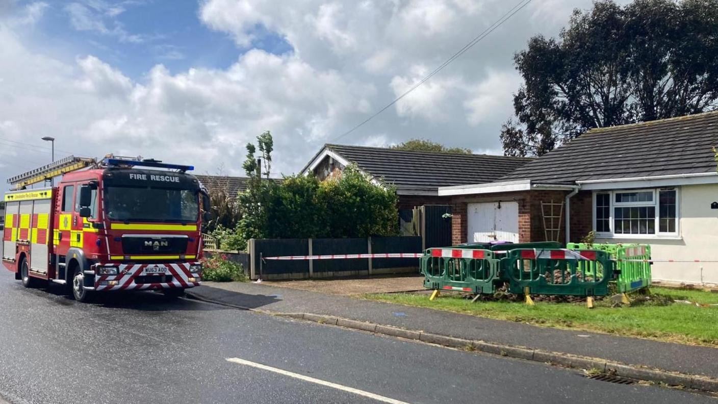 Fire engine outside bungalow, which has barriers standing in the front garden