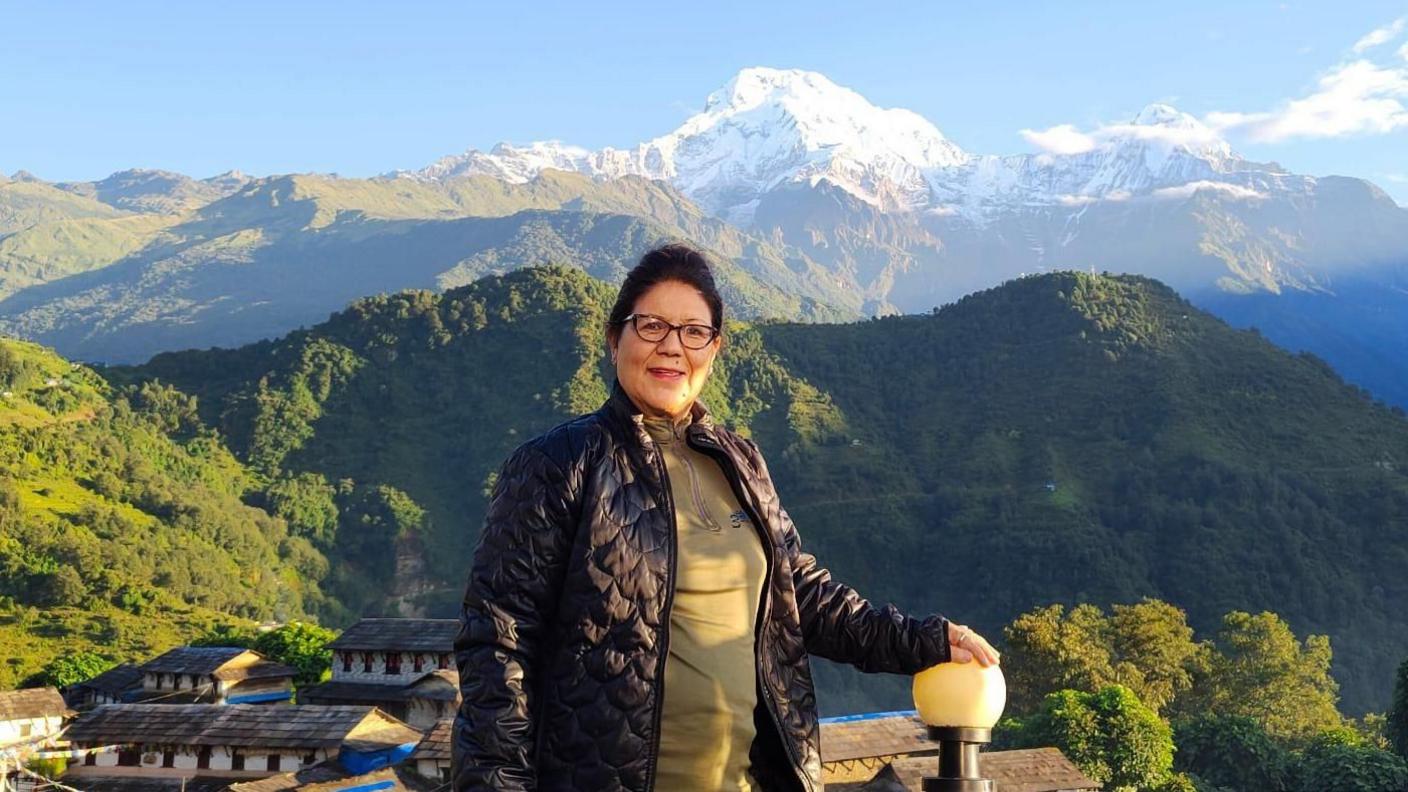 Lucky Chhetri, one of the pioneering women trekking guides in Nepal, poses in front of the Himalayas which can be clearly seen