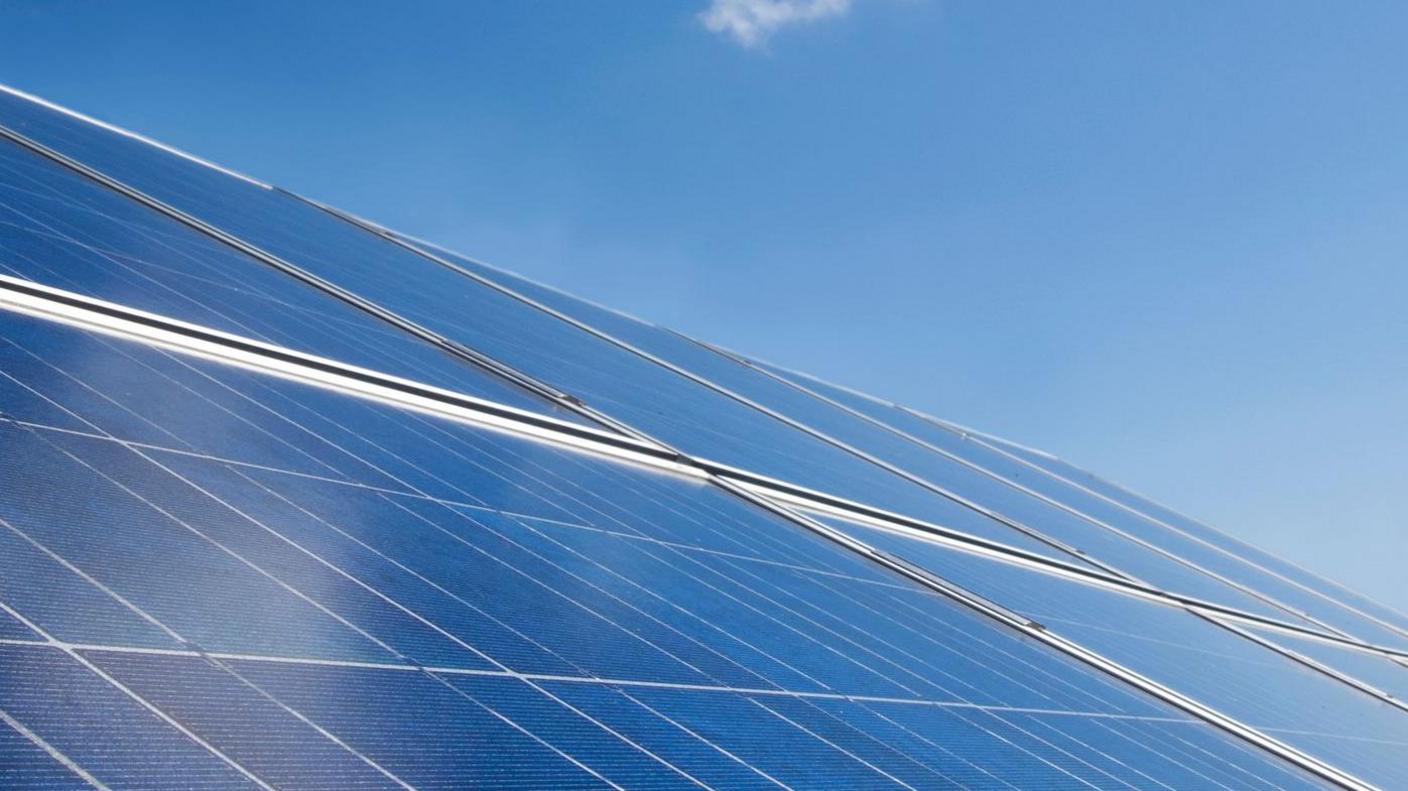 An aerial view of solar panels on the roof. The sky is blue and clear.