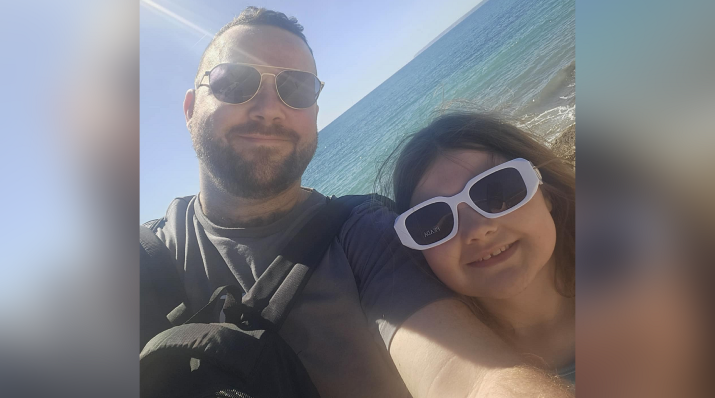 Chris Williams and his daughter. They are pictured on a beach in Majorca with the sea behind them. Chris has short dark hair and is wearing dark sunglasses. His young daughter has long dark hair and is wearing dark sunglasses with a white frame. Both of them are looking at the camera and smiling.