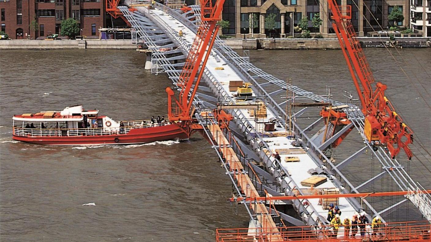 The bridge in construction, with orange machinery seen working on the structure.