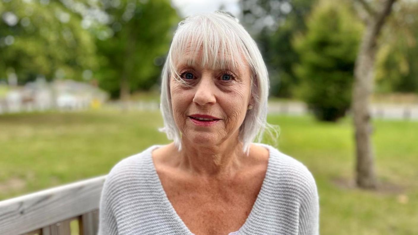 Karin Ronen wearing a grey cardigan and sat on a bench