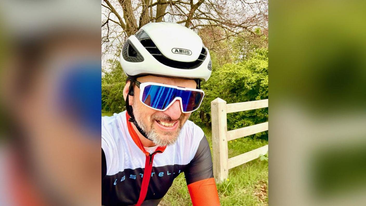 Stuart on his bike in a tight red, white and blue suit. He is wearing a helmet