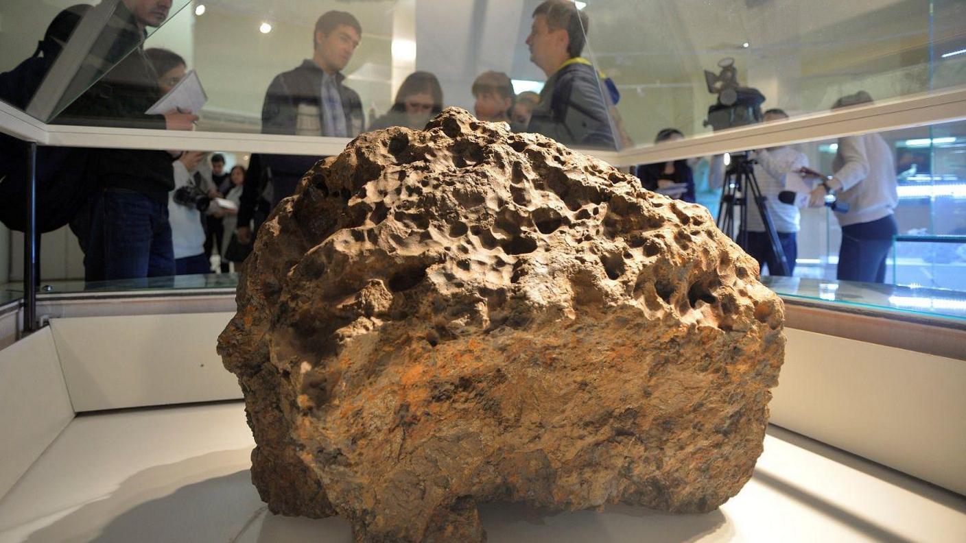 People looking at a piece of a meteorite at a museum in Chelyabinsk.