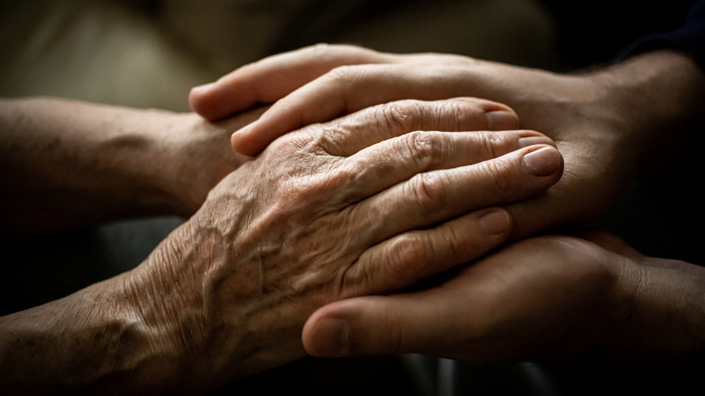 An elderly person holding hands with a younger person.