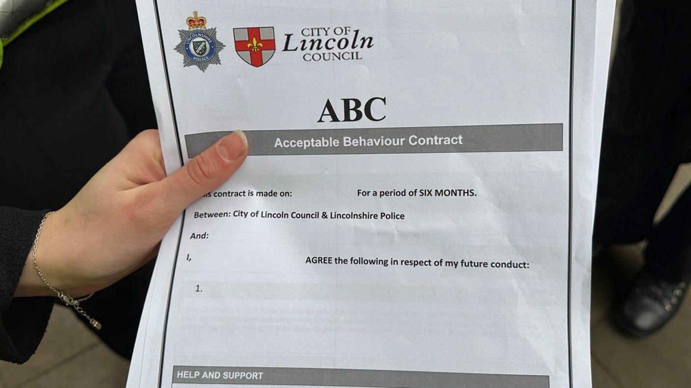 A person holding an ABC form, which includes headings for details about what a young person will agree to in respect of their behaviour. It has the emblems of Lincolnshire Police and the city council at the top of the document.