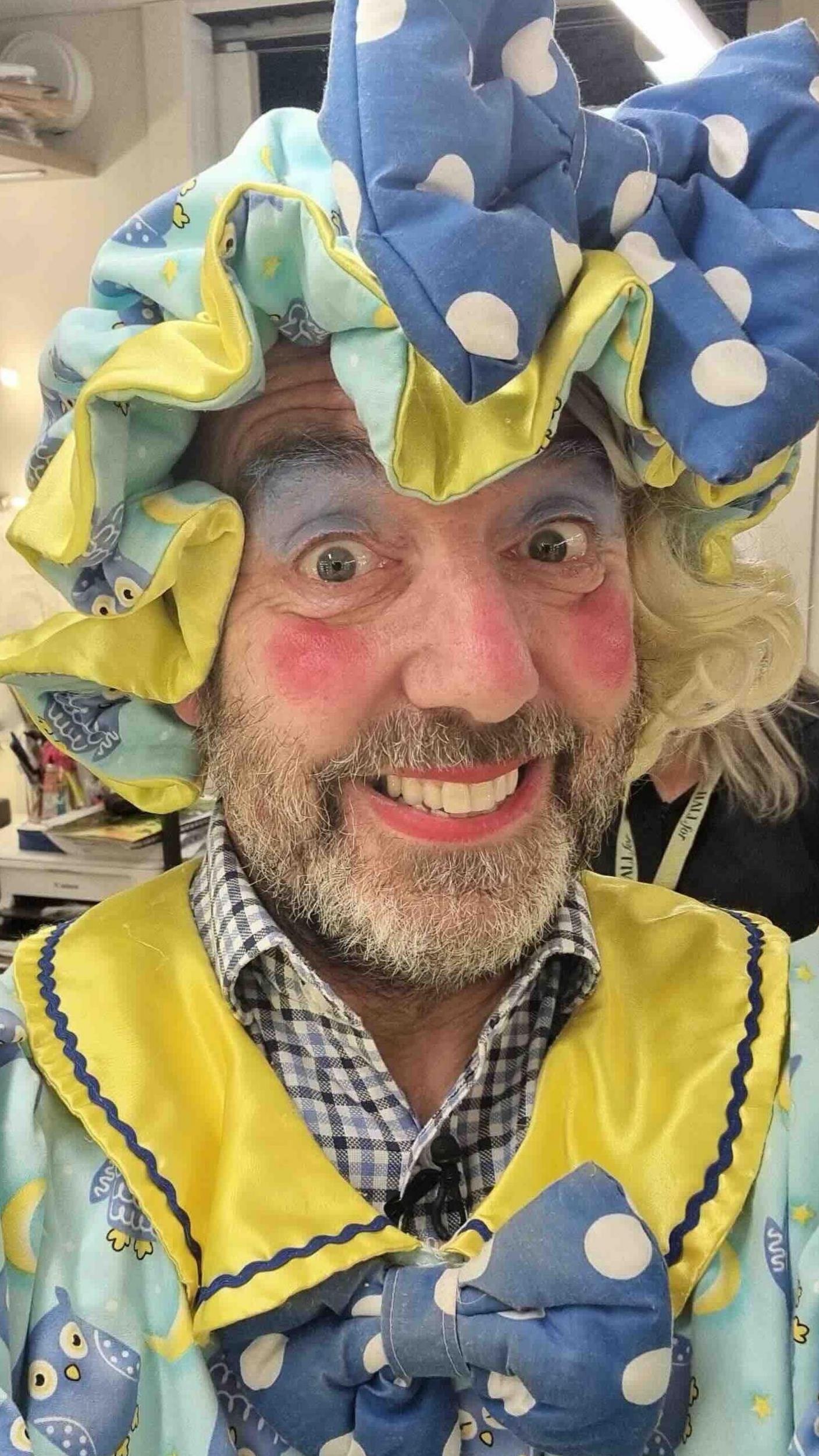 A pantomime dame with a yellow and blue outfit and a beard.