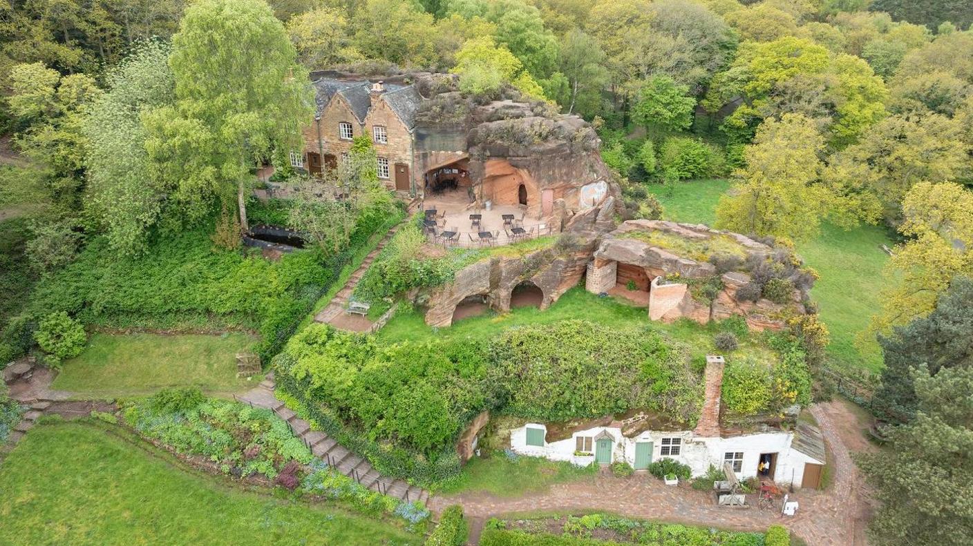 An overhead drone shot showing homes built into the side of a hill with doors and windows cut into the sandstone. Some openings of caves can be seen.