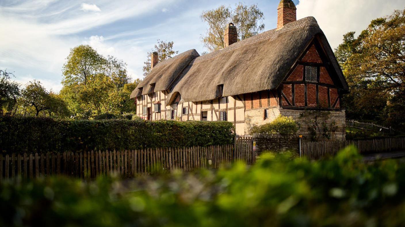 A large thatched house sits in a large garden.