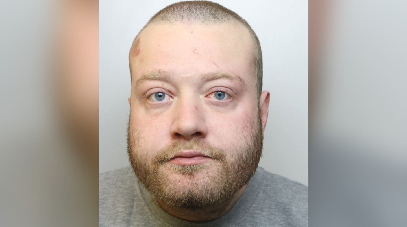 A custody image of Christopher Monro. He has a buzzcut and fair facial hair. He is looking directly at the camera with a blank expression and is wearing a grey sweatshirt or T-shirt. One of his eyes is slightly bloodshot. 