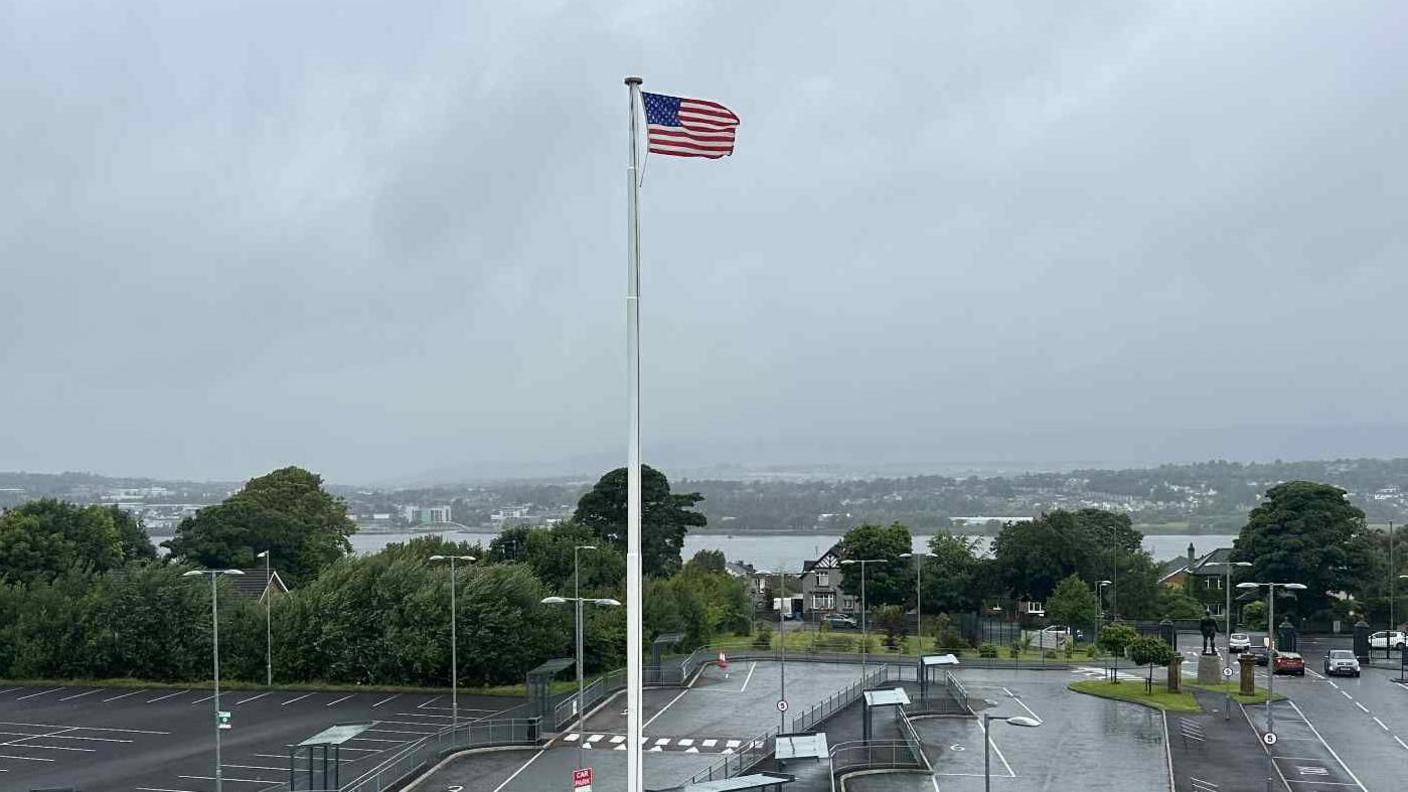 A US flag is pictured flowing in the wind on a large white flag pole.