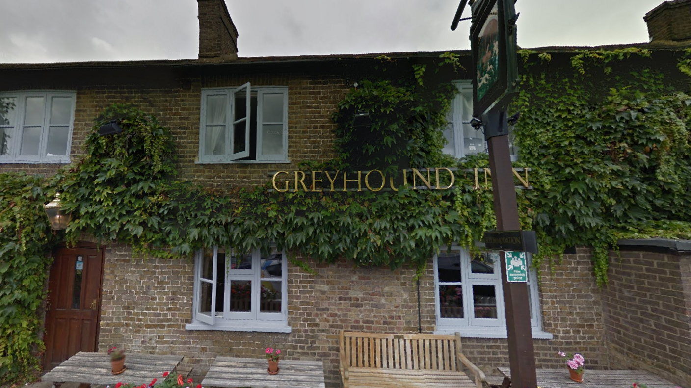 A view of the Greyhound Inn from outside via Google Streetview. There is a gold pub sign displaying the pub name. The building has two floors and is covered in green ivy.