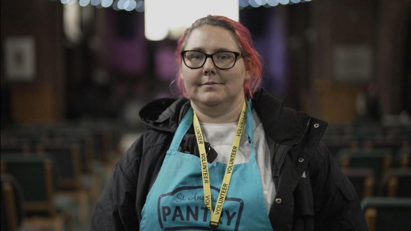 Maria, a food bank volunteer wearing a blue apron and a black coat