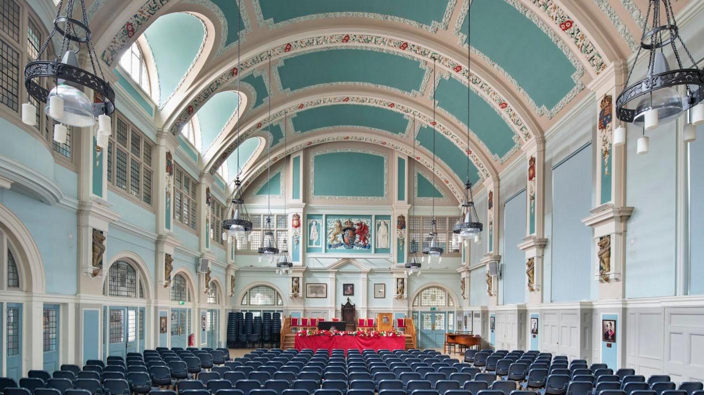 A central hall with pale blue and green walls and ceiling with blue chairs and ornate plasterwork