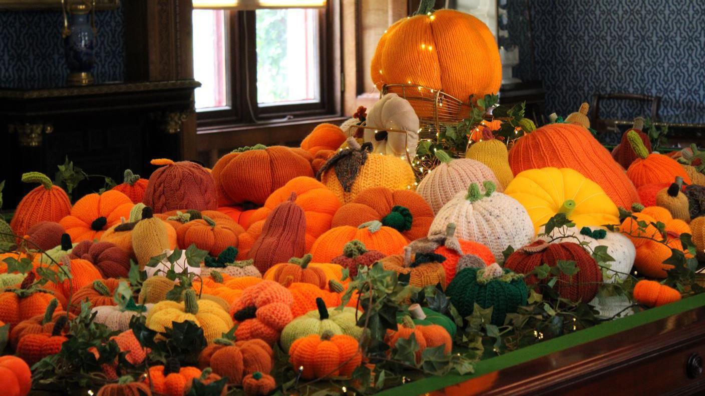 Hundreds of brightly coloured knitted pumpkins and seasonal autumnal vegetables piled up on a tabletop in a kitchen.
