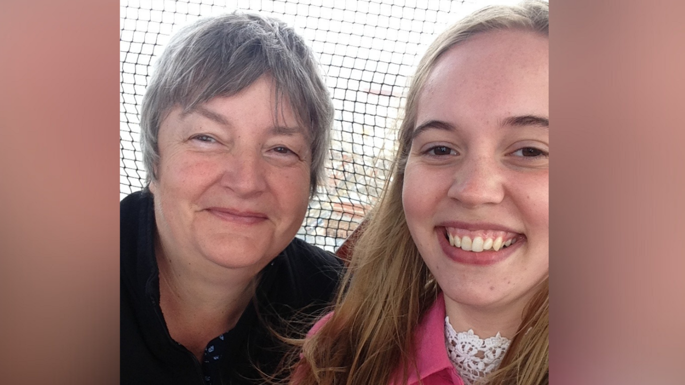 A woman on the left with short grey hair, wearing a dark top. On the right is a younger woman with long brown hair and a red top. They are both smiling.