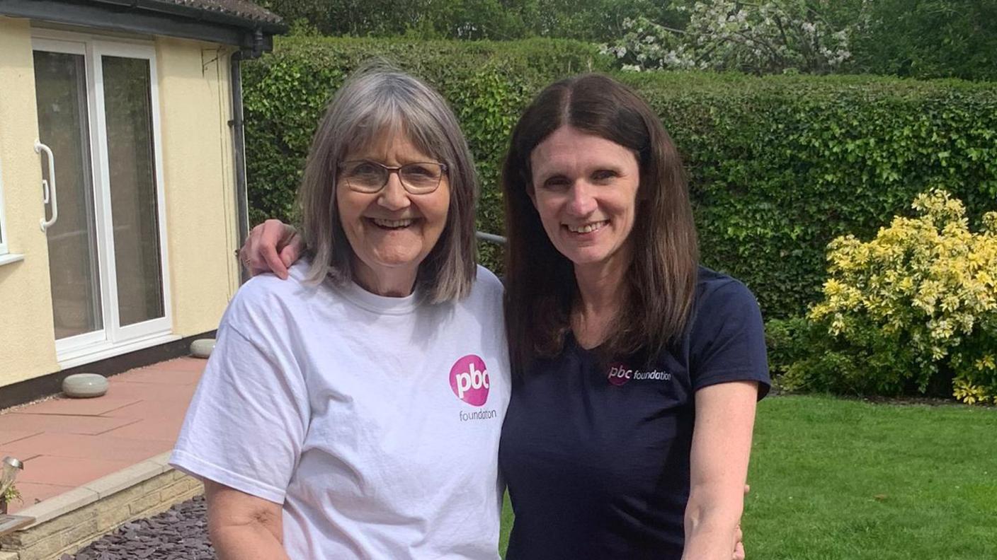 Gill Rich wearing a white T-shirt with a logo for the PBC Foundation and Wendy Wheat wearing a dark blue T-shirt with a PBC Foundation logo. 