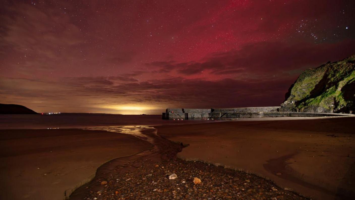 A beach scene with a pink sky and some cloud cover