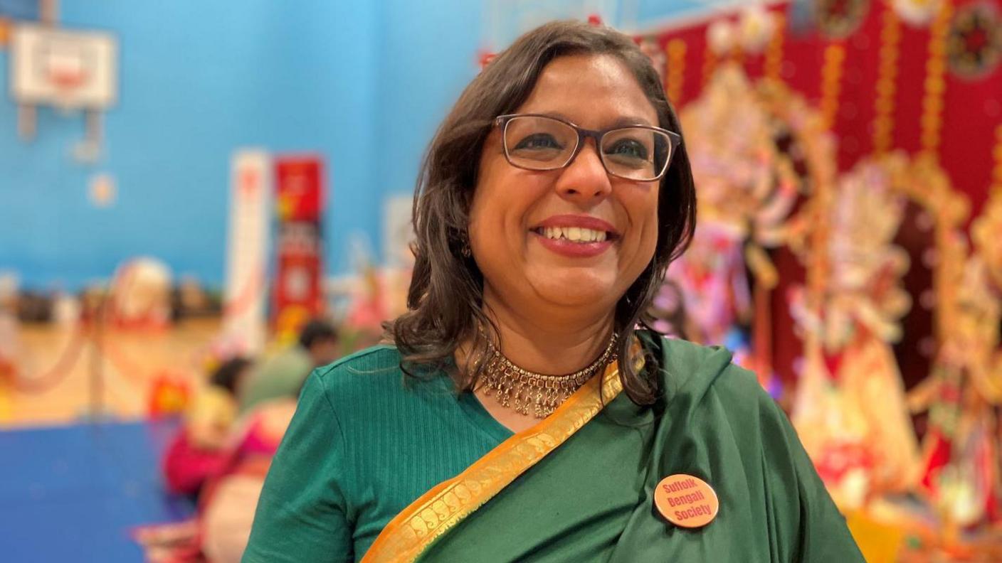 Sue Raychaudhuri stands in front of the Durga Puja icons, she is wearing traditional Bengali dress