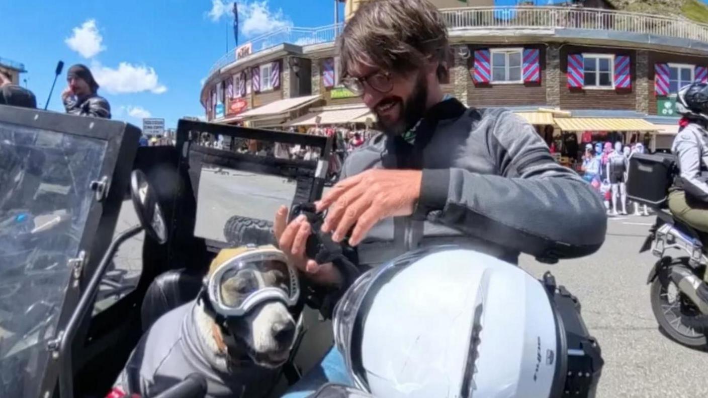 A man sitting with his dog in a sidecar on the side of the road