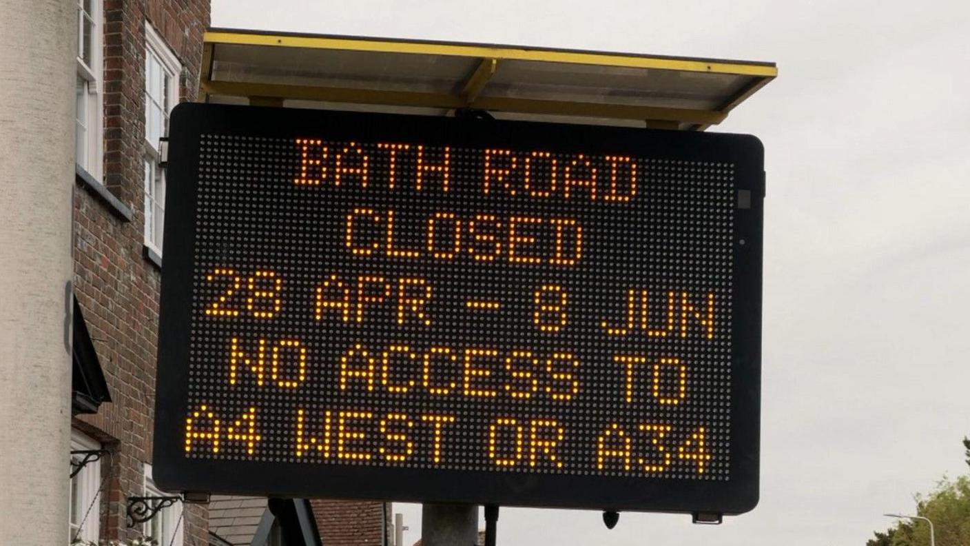 A digital road sign has been lit-up to read "Bath Road closed 28 Apr - 8 Jun. No access to A4 west or A34".  Houses can be seen behind the sign and grey skies overhead.