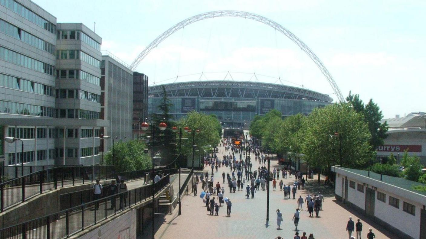 Exterior shot of Wembley Stadium with its arch and people walking on the concourse approaching the stadium for the FA Vase final in 2008