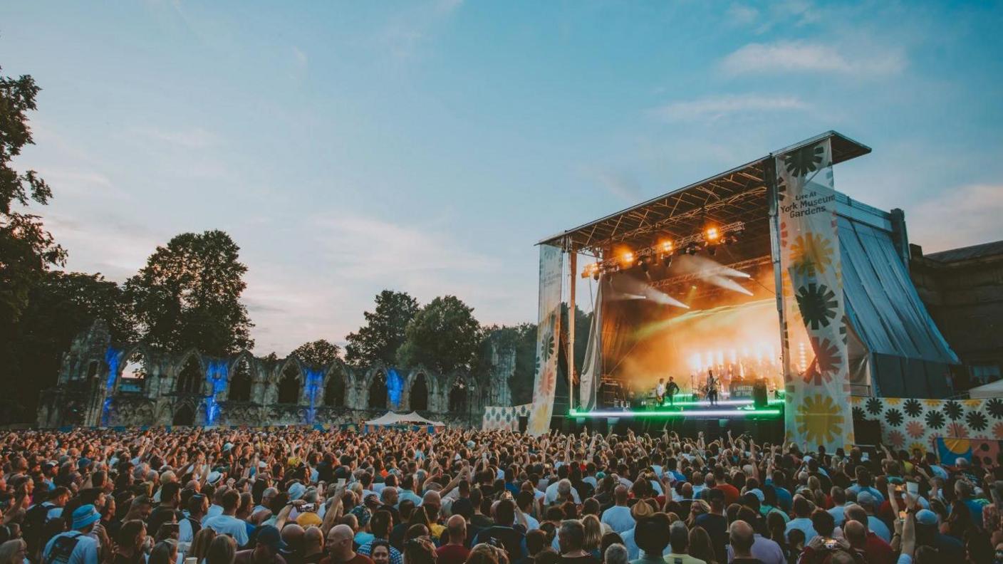A crowd of people watch a band perform in York's Museum Gardens.