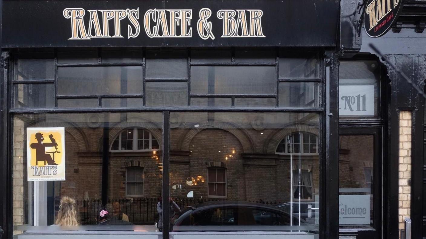 The exterior of Rapp's Cafe & Bar. It has a large glass window while the frames and walls are painted black with a logo in gold above.