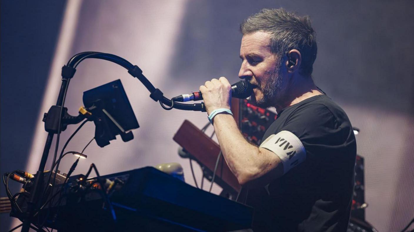 Robert Del Naja of the British Trip Hop collective Massive Attack performs on the Lake stage during the Montreux Jazz Festival in Switzerland. He can be seen holding a microphone over a mixing board.