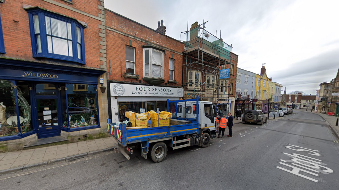 A row of shops on Glastonbury high street, with van and cars parked outside.