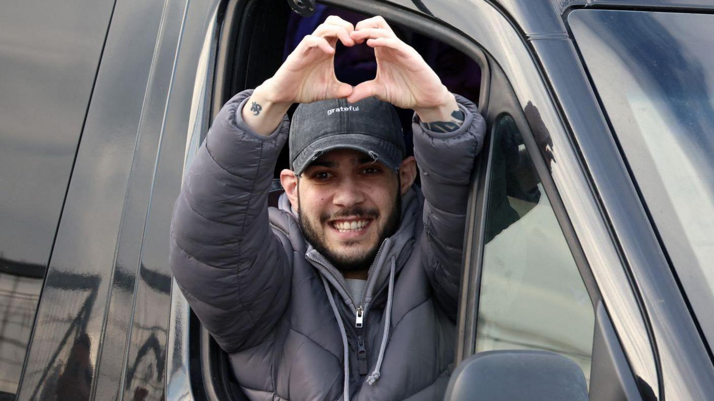 Eliya Cohen smiles after being released on February 22. He is holding up his hands to form a heart symbol
