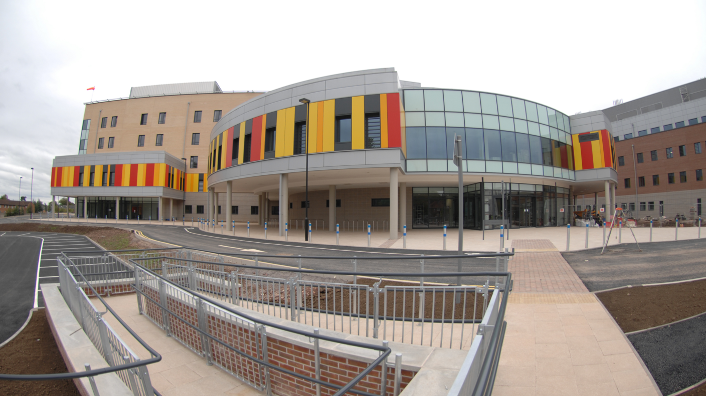 The outside of Royal Stoke University Hospital. It is a curved like building with yellow, orange and red panels on the outside. 