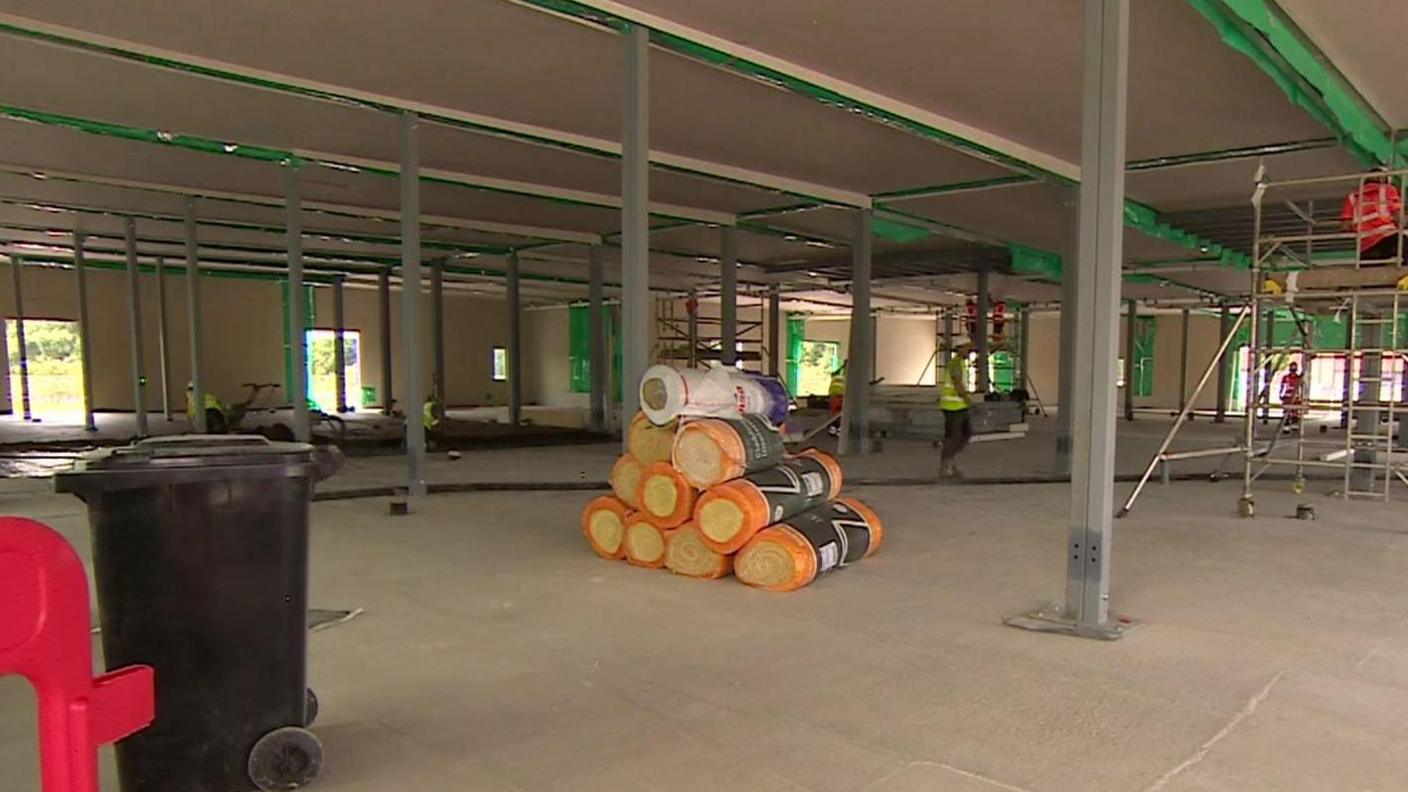 Inside one of the community diagnostic centres. It looks like a building site with scaffolding visible and workers in hi-vis jackets