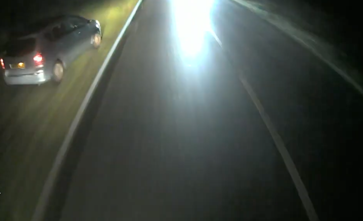 Blurry dashcam screencap of a silver car that's swerved onto a grass verge at the side of a road.